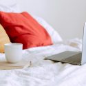 a cup of tea next to an open laptop on the bed