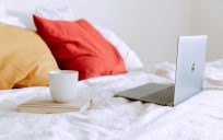 a cup of tea next to an open laptop on the bed