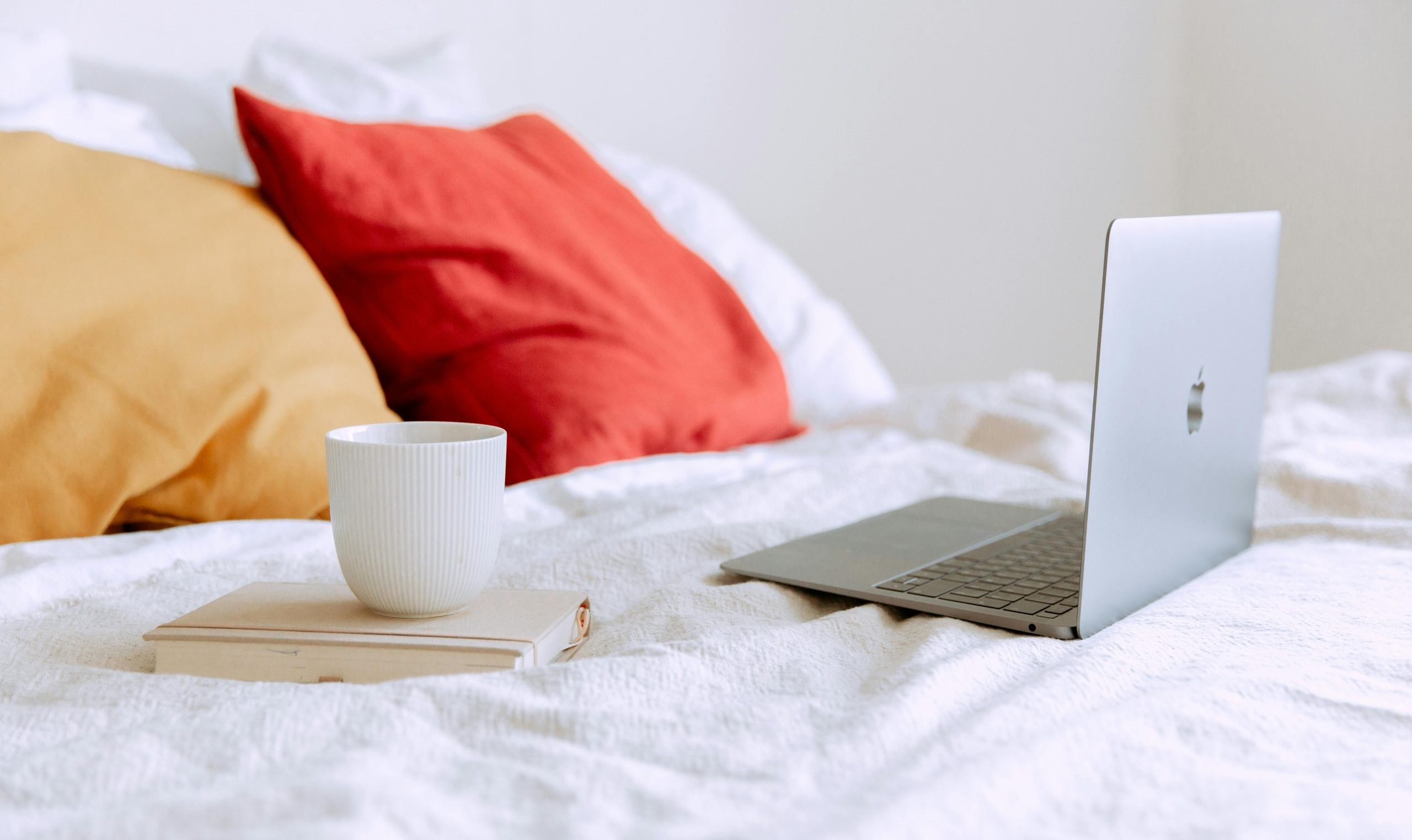 a cup of tea next to an open laptop on the bed